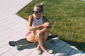 Smiling fit woman relaxing while sitting on a longboard in the park for skating.