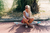 Happy athletic woman sits on a longboard resting in the shade on a hot summer day after a workout.