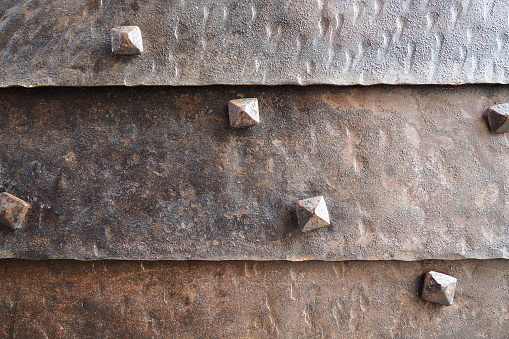Background of metal surface from sheets with rivets, close-up. Texture of the iron gate. A metal relief backing for branding. Herceg Novi, Montenegro. Metal pimples. Gate of a fortress or castle