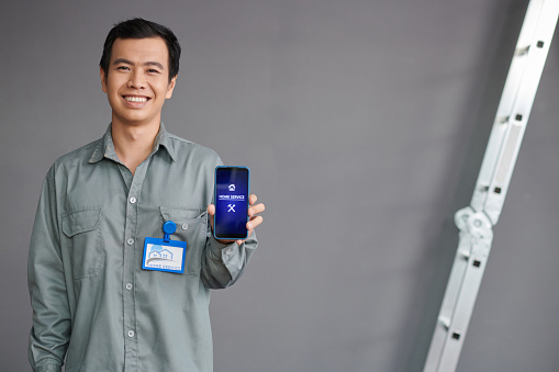 Portrait of cheerful home service worker showing smartphone with mobile application