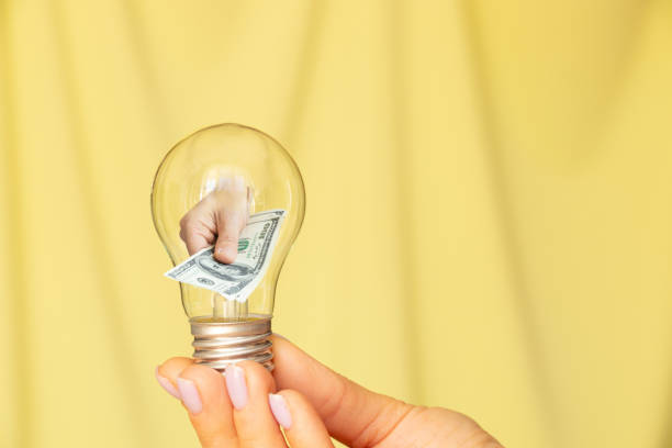 istock A woman's hand holds a light bulb and the second hand gives dollars from a light bulb on a yellow background, income and profit 1514352528