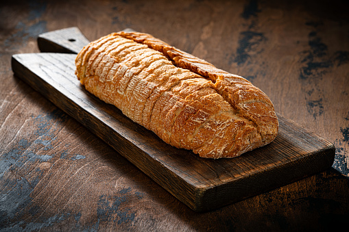 Bread loaf sliced on a wooden cutting board over wood rustic table low key
