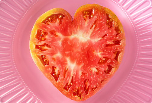 Heart shape Fresh tomato half cut macro closeup texture detail on a pink plate mediterranean food