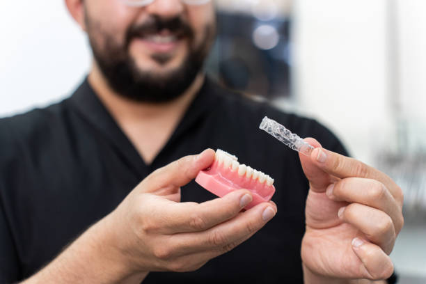 istock Smiling doctor installing clear aligners on plastic human jaw model presenting teeth correction 1514424614