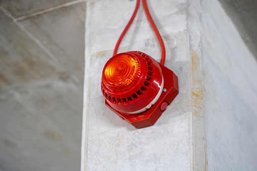 One single simple red alert alarm light on a concrete wall, underground parking lot, metro station, industrial production hall emergency stop light. Danger indicator, red stop light, safety, security