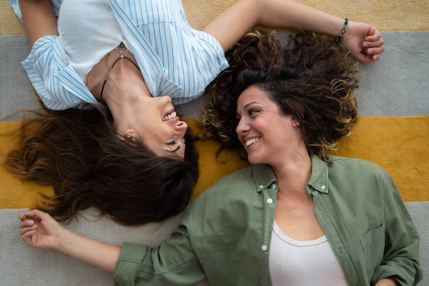 istock Two smiling young women looking at each other while lying on the floor at home 1514669578