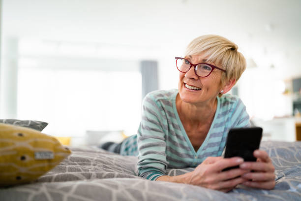 istock Elderly blonde female holding phone and lying down on bed 1514697812