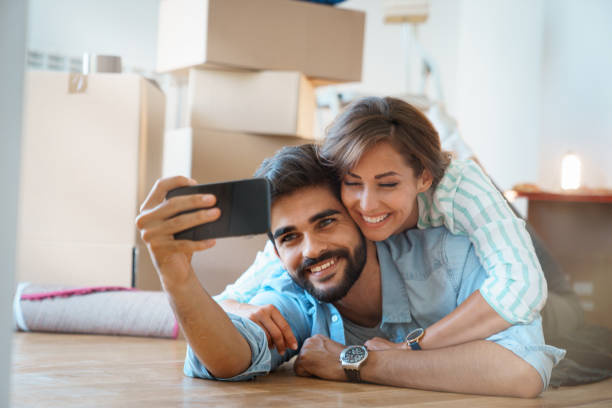istock Happy young couple in love using mobile phone in new apartment while lying on floor 1514707978