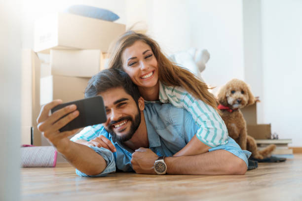 istock Cheerful young couple in love using mobile phone in new apartment while lying on floor with dog 1514708392