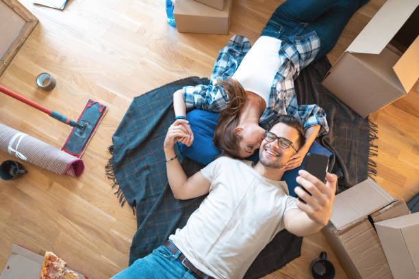 istock Young couple using mobile phone while lying on the floor at their new apartment 1514748111