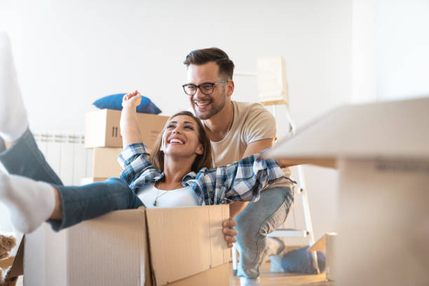 istock Happy young man with eyeglasses having fun with his girlfriend while pushing her in carton box at their new home 1514757691