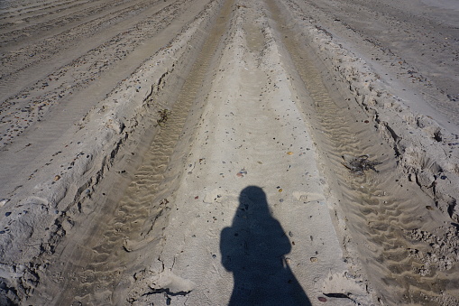Tire tracks in the sand. The photographer's shadow on the sand. The shadow of a girl on the sand. The shadow of a photographer girl on a sandy beach.