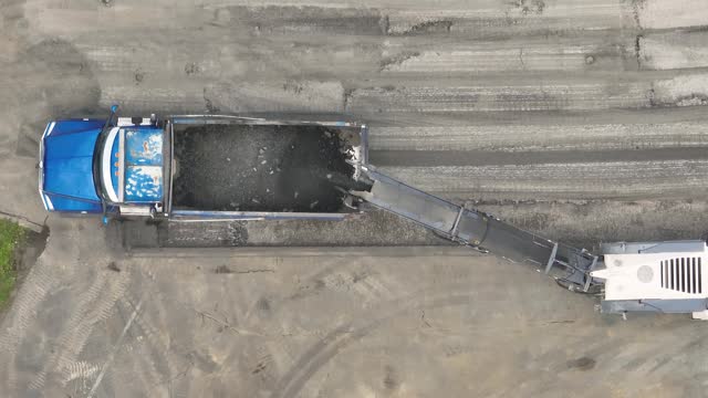 Aerial view of a road milling machine removes old asphalt and loads milled asphalt into the dump truck.