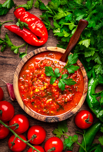 Traditional armenian spicy adjika sauce with hot pepper, paprika, tomatoes, garlic and parsley on rustic wooden kitchen table background, top view