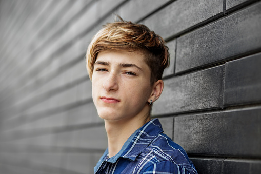 Portrait of caucasian young man teenager looking at the camera. Gray wall. Urban people style. Gen Z. Close up