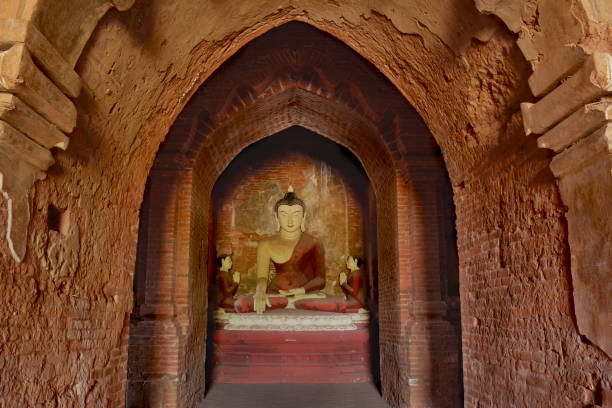 Lord Buddha sculpture sitting in meditation inside ancient temple in Bagan, Myanmar. Praying monks statues on the right and left sides from Buddha.