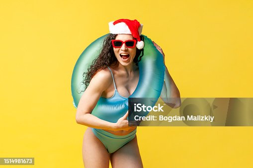 istock attractive girl in swimsuit and sunglasses in santa hat and with an inflatable swim ring smiles on yellow background 1514981673