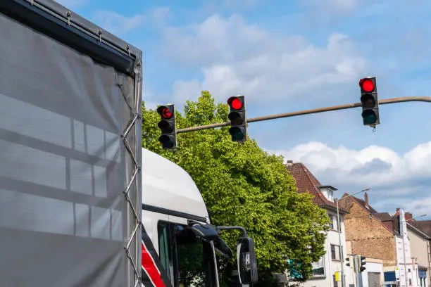 Photo of Part of the cabin of a truck standing at an intersection in front of red traffic lights.