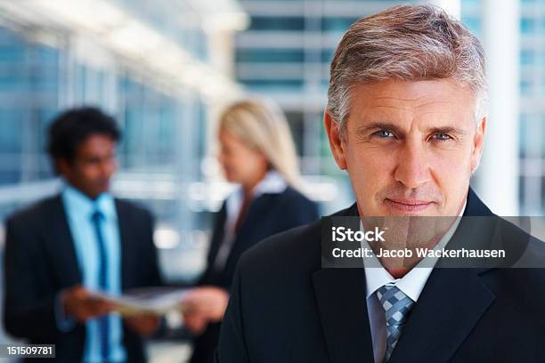 Mature Businessman With Colleagues In The Background Stock Photo - Download Image Now