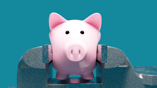 Distorted pink piggy bank squeezed in vise , symbolizing financial stress and debt. with plain blue background