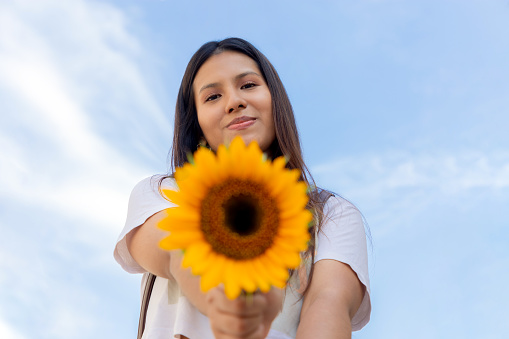 young woman, smiling and holding a sunflower on a sunny spring day in a park, selective focus, concept of joy, and beauty in spring. peace, giant yellow sunflowers.