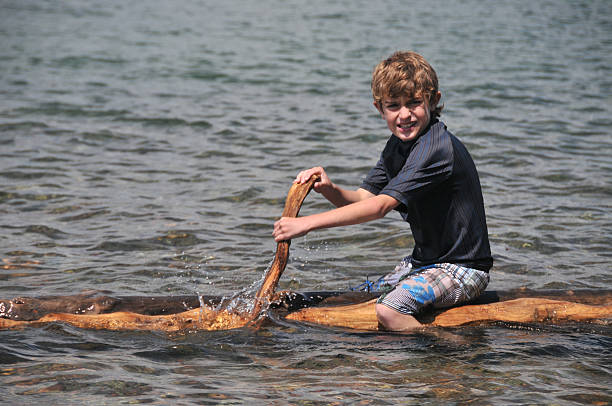 Boy paddles a home made raft on a lake.