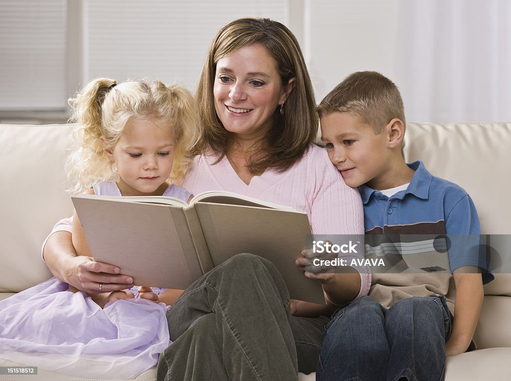 Happy Mother Reading to Children A happy-looking mother reading to her son and daughter in their home.  Horizontally framed shot. Adult Stock Photo