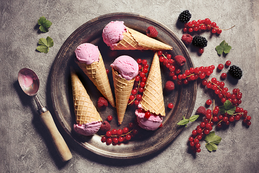 Pink ice cream with cones and berry fruits on rustic plate