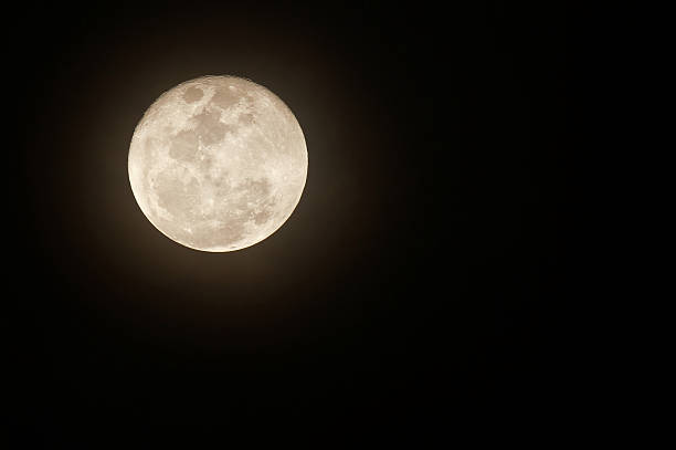 Glowing full moon against black night sky stock photo