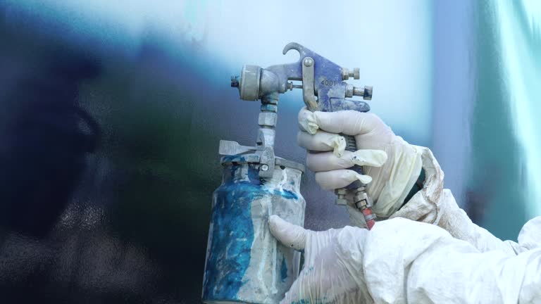 A worker in a body protective suit paints the hull of a sailing yacht with spray.