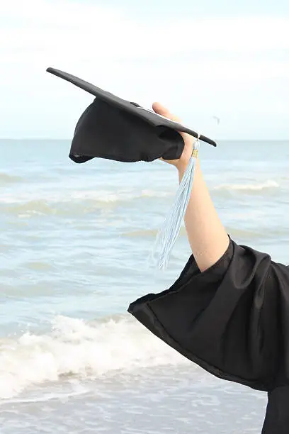 Graduation cap in hand with Ocean background