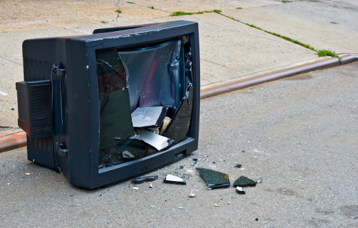 Old smashed television set sitting on the side of the road
