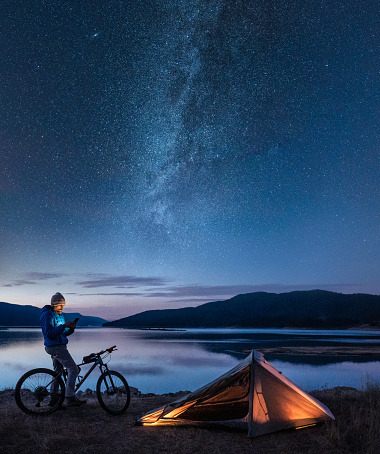 Man on bike adventure trip with tent near lake at night.