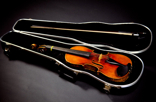 Three quarter sized violine in black case on black background.