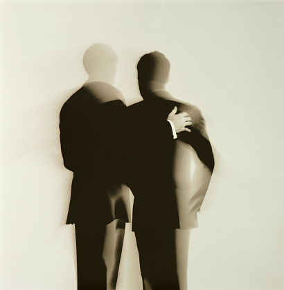 Rear view of two businessmen looking down at something one is holding - one has his hand on the other ones shoulder. Abstract silhouette 