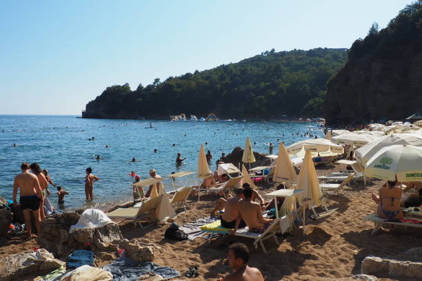 Sand and pebble beach near high cliffs. Beach umbrellas, cafes, deck chairs. People relax, swim, enjoy and sunbathe. Tourism business in the Balkans. stock photo