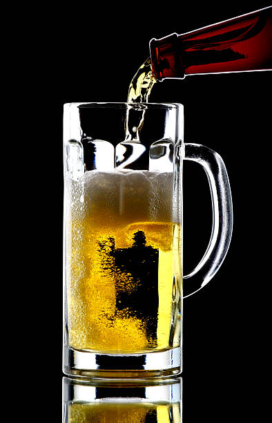 Beer flows from bottle in a glass on  black background stock photo