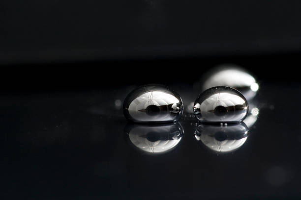 Three drops of mercury lying on a black surface Shiny Mercury drops on a pit black background mercury metal stock pictures, royalty-free photos & images
