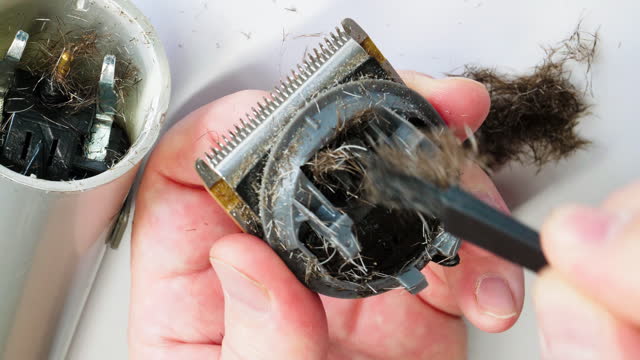 Repairman cleaning hair clipper. Cleaning the trimmer from hair. Hands clean the clipper with a brush. Hairdresser repairs equipment for a professional haircut. Close-up. Barbershop tool. Slow motion