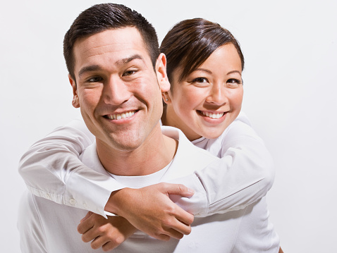 An attractive young couple posing together.  They are smiling directly at the camera.  Horizontally framed shot.