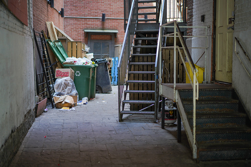 An alley was in Old Montreal, QC Canada with trash and recycling bins and two stairways.