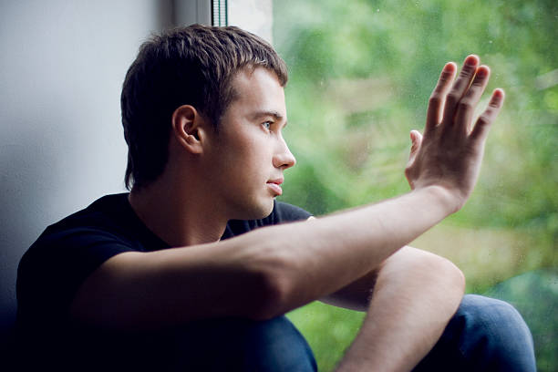 istock Man looking out a window and placing his hand on the glass 151534035