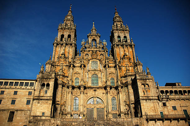Front view of Santiago de Compostela Cathedral framed by curved stone arch. Obradoiro town square, incidental unrecognizable people, clear sky background.