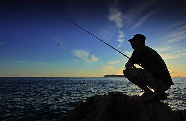 Photo of Person fishing during the sunset on a vast body of water