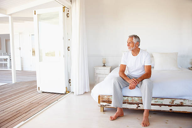 contemplative senior homme assis sur le lit - homme 65 ans photos et images de collection