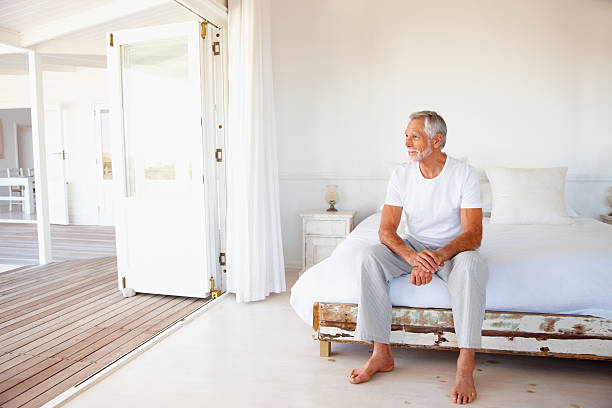 contemplative senior man sitting on bed - 僅老年男人 個照片及圖片檔