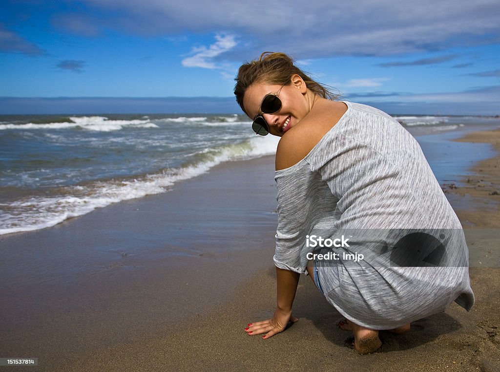 Young girl at the beach Young happy girl at the beach, kneeling down and looking over her shoulder at the camera. Adult Stock Photo