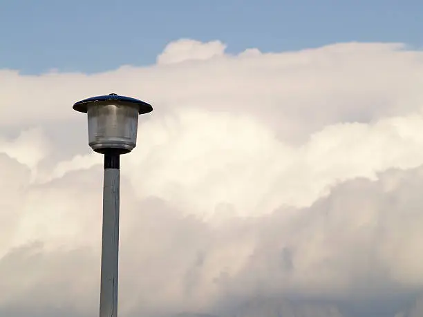 Simple landscape composition of a lampstand set against stormy clouds and blue sky above.