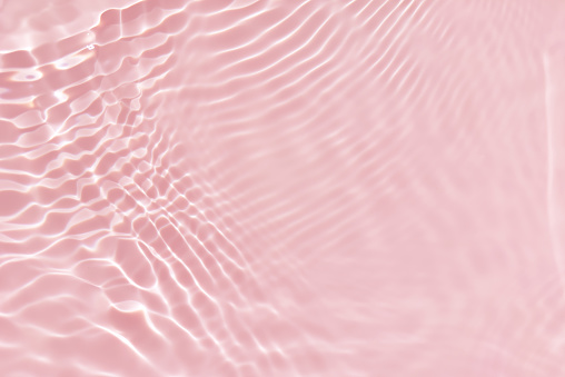 Pink water with ripples on the surface. Defocus blurred transparent white colored clear calm water surface texture with splashes and bubbles. Water waves with shining pattern texture background.