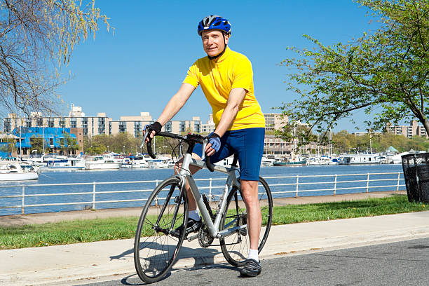 Caucasian senior man sitting on a road bike.  He's wearing a helmet and cycling clothing. - See lightbox for more